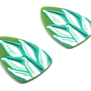 May include: A pair of green and white leaf-shaped earrings with a white background and green leaf pattern.