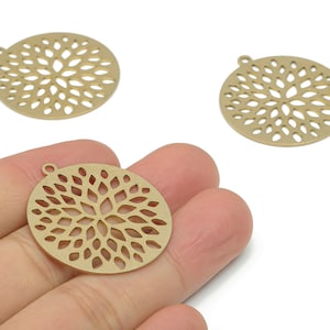Peut inclure: Trois breloques circulaires en métal doré avec un motif floral. Une breloque est tenue dans une main. Chaque breloque a une petite boucle en haut pour l'attacher à des bijoux ou autres créations. Les breloques mesurent environ 3,8 cm de diamètre.