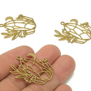 Puede incluir: Encantos de metal dorado con un diseño celestial. Cada dije presenta una forma de cristal, una luna creciente, estrellas y ramitas de hojas. Un dije se sostiene en una mano, con otros dos visibles en el fondo. Ideal para la fabricación de joyas.