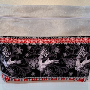 May include: A white zippered pouch with a silver glitter finish. The front of the pouch features a black and white reindeer print with snowflakes and a red and white trim.