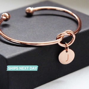 Rose gold colour bracelet with an initial charm, J on the bangle which is put on the black gift box