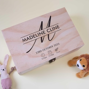 May include: A light wooden keepsake box with the name "Madeline Cline" and birth details printed on the lid. The box features a decorative "M" initial, date, time, weight (4.12 kgs), and length (51cm). A plush lion and bunny toy are in the image.