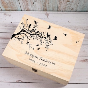 May include: A wooden keepsake box featuring a black silhouette of a tree branch with birds flying away. The box is engraved with the text "Morgan Anderson 1945 - 2024".