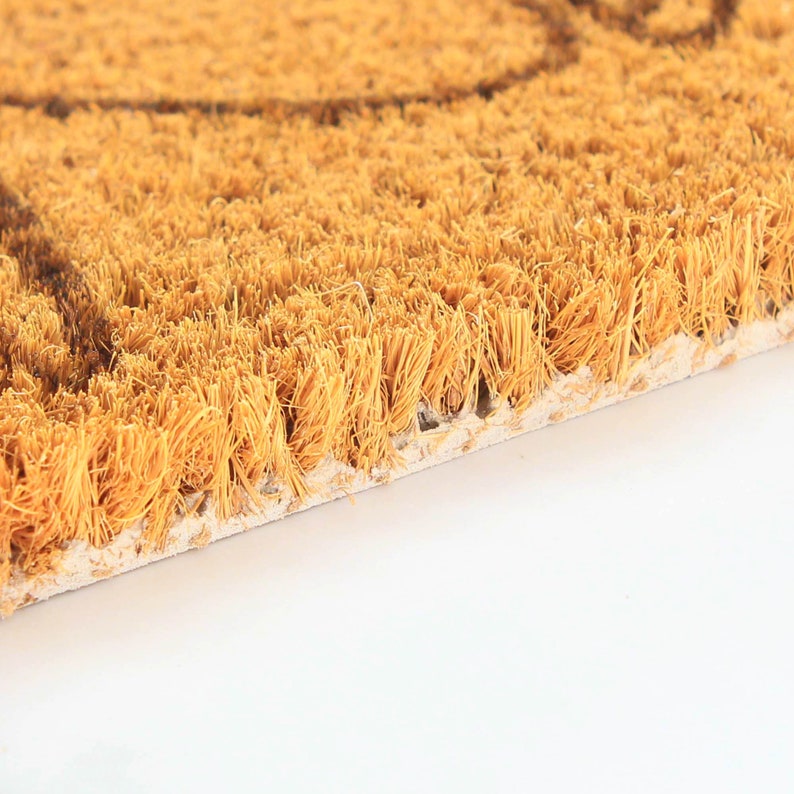 May include: Close-up of a brown coir doormat with a textured surface. The fibers are tightly woven and the mat has a natural, rustic look.