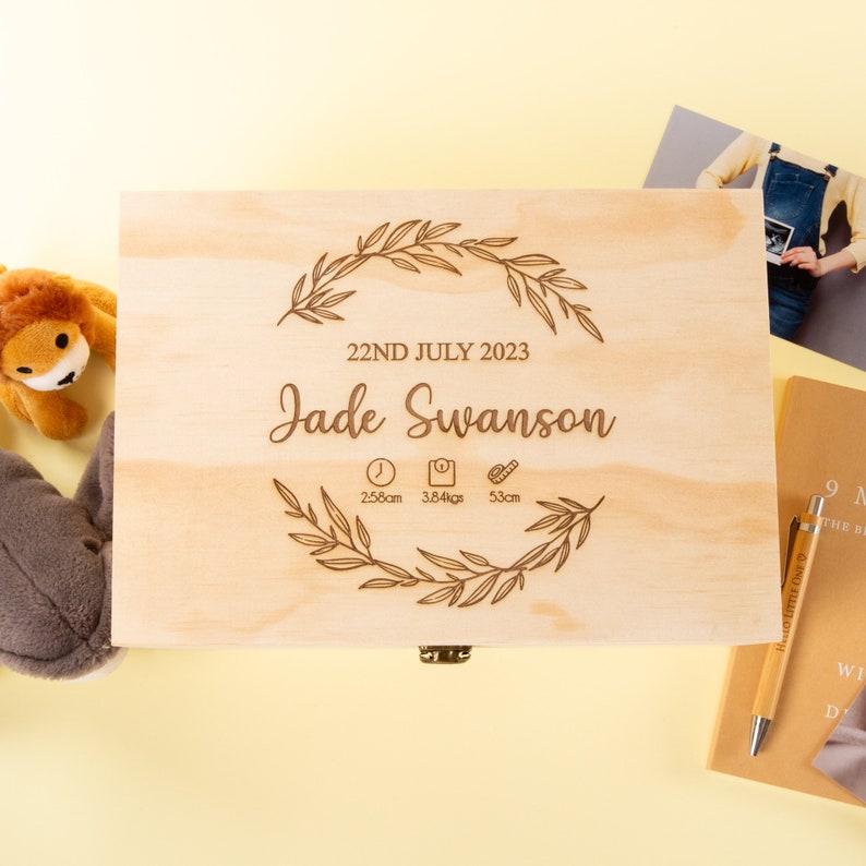 May include: A wooden keepsake box with an engraved design featuring a leafy wreath, the date "22ND JULY 2023", the name "Jade Swanson", and the baby's birth stats: 2:58am, 3.84kgs, and 53cm.