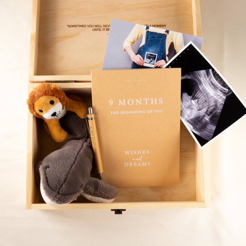 May include: A wooden box with a brown journal that says "9 Months, The Beginning of You, Wishes and Dreams". The box also contains a stuffed lion, a stuffed whale, a pen, and a black and white ultrasound image.