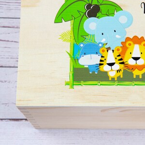 May include: A wooden box with a colorful jungle scene featuring a blue elephant, a blue hippopotamus, a yellow tiger, and an orange lion. The box is made of natural wood and has a hinged lid.