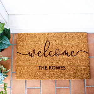 May include: A brown coir doormat with the word "welcome" written in cursive script and the text "THE ROWES" below it.