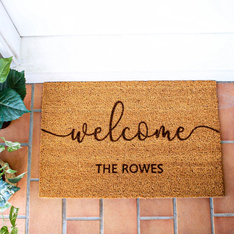 May include: A brown coir doormat with the word "welcome" written in cursive script and the text "THE ROWES" below it.