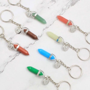 May include: Seven crystal keychain charms with silver key rings and letter charms. The crystals are green, orange, white, blue, green, brown, and red.