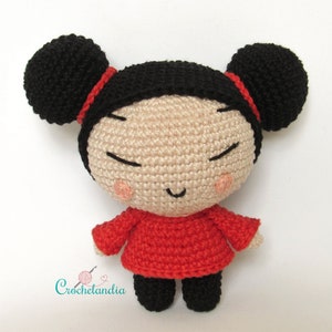 May include: A crocheted amigurumi doll with black hair in two buns, a red dress, and a smiling face.