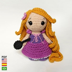 Peut inclure: Poupée au crochet faite à la main avec de longs cheveux dorés et une robe violette. La poupée a un accessoire noir et une fleur rose dans les cheveux. La poupée est faite avec un point de crochet et a de grands yeux noirs.