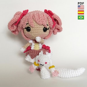 Pode incluir: Boneca de crochê feita à mão com cabelo rosa e uma roupa combinando, segurando uma pequena criatura branca. A boneca tem olhos pretos e detalhes vermelhos. A imagem inclui um ícone PDF e bandeiras.