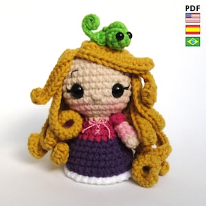 May include: A crochet doll with long golden yarn hair, large black eyes, and pink cheeks. The doll wears a pink and purple dress with white trim and has a small green crocheted chameleon perched on top of its head. The design is a handmade toy.