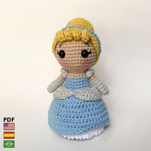 Puede incluir: Muñeca de ganchillo hecha a mano de una princesa con un vestido azul y una enagua blanca. La muñeca tiene cabello rubio, una diadema azul y guantes grises. La cara de la muñeca tiene mejillas rosadas y ojos negros. El patrón es PDF.