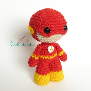 Peut inclure: Un jouet en peluche crocheté de Flash, un super-héros avec un costume rouge et jaune. Le jouet a un masque rouge avec un éclair jaune sur la poitrine.