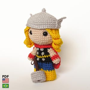 May include: A handmade crochet doll of Thor, featuring a gray helmet, yellow hair, and a red, black, and blue outfit. The doll holds a gray hammer. The doll is approximately 6 inches tall.