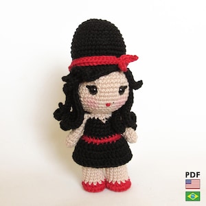 May include: A handmade crochet doll with black hair, a black dress with red trim, and red shoes. The doll wears a black hat with a red band. The doll has a light skin tone and a sweet expression.