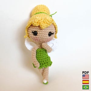 Puede incluir: Una muñeca de hada de ganchillo hecha a mano con cabello amarillo, vestido verde y alas blancas. La muñeca tiene ojos negros y un tono de piel claro. La muñeca está hecha de hilo y es un artículo artesanal caprichoso.