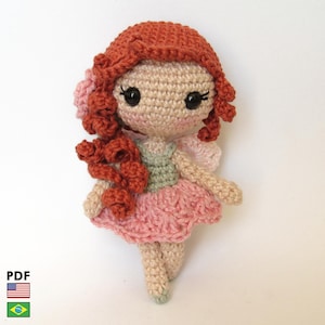 May include: A handmade crochet fairy doll with red hair, a pink dress, and small wings. The doll has a light skin tone and is wearing a green top. The doll is a whimsical, handcrafted item.