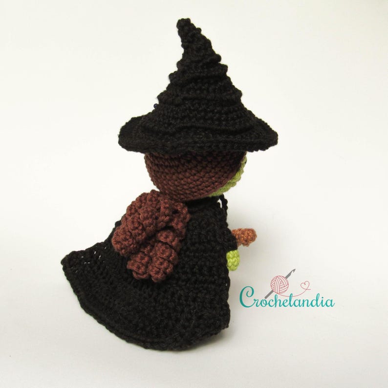 May include: A handmade crochet witch doll, featuring a black pointed hat and matching cloak. The doll has a brown head, a green face, and a brown and orange broom. The doll is a whimsical, handcrafted item.