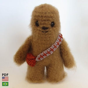 May include: A handmade brown plush toy resembling a character from a science fiction film. The toy has a bandolier with red and gray accents and a small red pouch. The toy has black eyes and a stitched mouth. The toy is made of soft, fuzzy material.