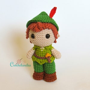 Pode incluir: Um boneco de Peter Pan de crochê com um chapéu verde, cabelo castanho e um traje verde. O boneco está usando um cinto marrom e sapatos marrons.