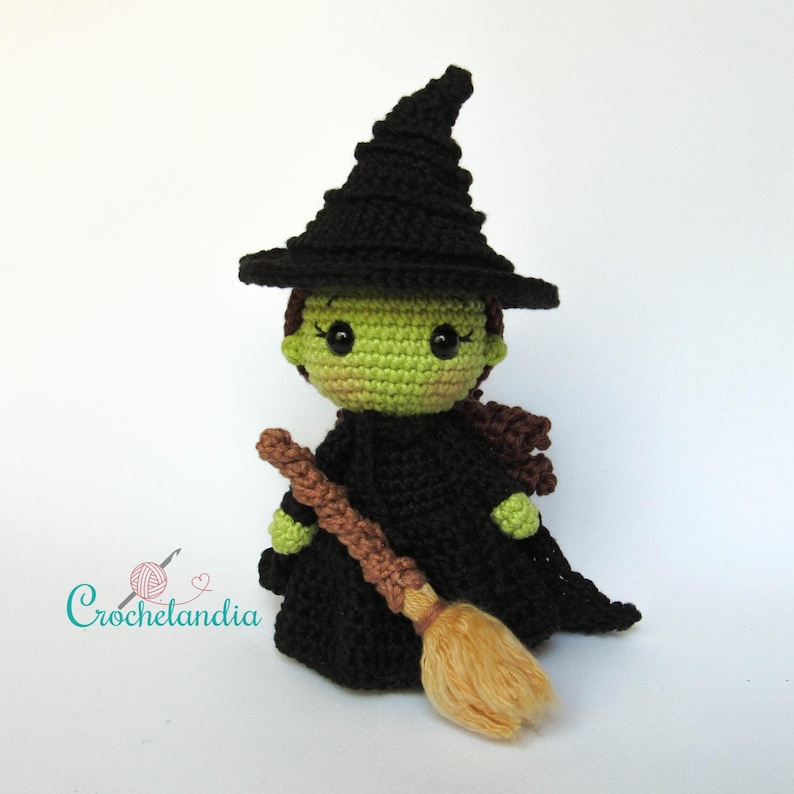 May include: A handmade crochet witch doll with a black hat and dress, green skin, and a brown broom. The doll has a whimsical design, perfect for Halloween or as a decorative item. The doll is approximately 6 inches tall.