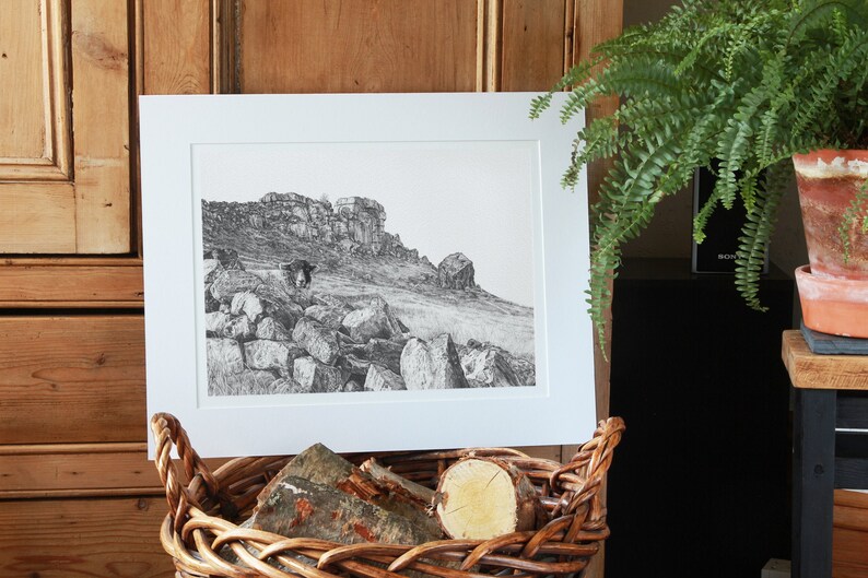 Pu&ograve; includere: Un disegno in bianco e nero di un paesaggio roccioso con una singola figura in primo piano. Il disegno &egrave; incorniciato con un passepartout bianco e una cornice bianca.