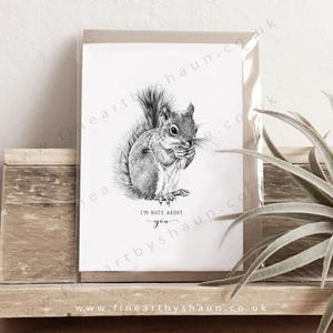 May include: A black and white illustration of a squirrel on a greeting card. The squirrel is holding a nut and the text "I'm nuts about you" is below the image. The card is in a clear plastic sleeve.