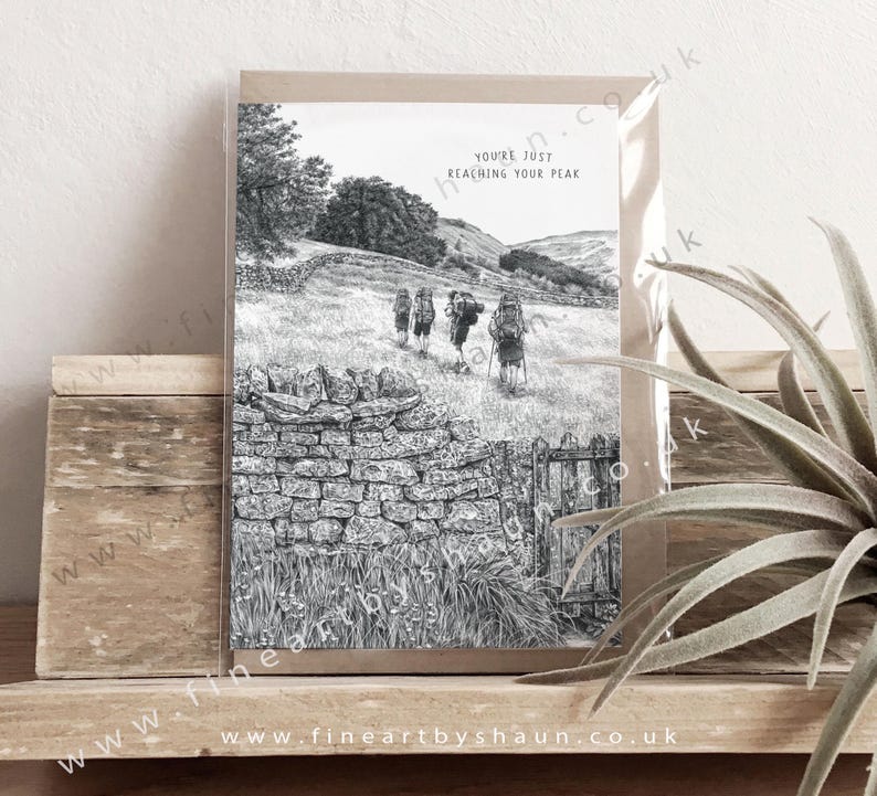 May include: Black and white illustration of a group of hikers walking on a path with a stone wall and a gate. The text "You're just reaching your peak" is printed on the card.
