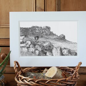 Pu&ograve; includere: Un disegno in bianco e nero di un paesaggio roccioso con una mucca in piedi in primo piano. Il disegno &egrave; incorniciato in una cornice bianca ed &egrave; esposto su una superficie di legno.