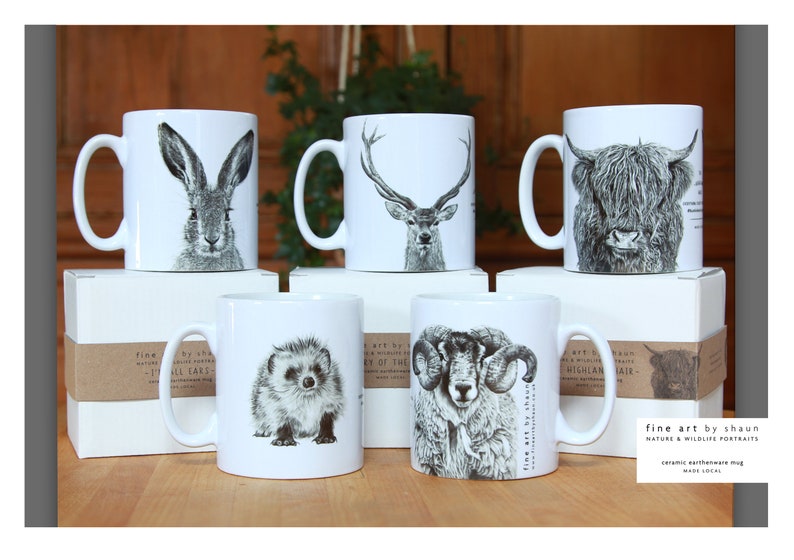 Pu&ograve; includere: Sei tazze in ceramica bianca con illustrazioni in bianco e nero di vari animali, tra cui una lepre, un cervo, una mucca delle Highlands, un riccio, un ariete e un'altra mucca delle Highlands. Le tazze sono disposte in due file da tre, con la fila inferiore che poggia su scatole con etichette di carta marrone che recitano "fine art by shaun nature & wildlife portraits ceramic earthenware mug made local".
