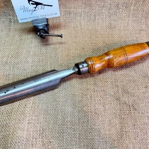 Peut inclure: Un ciseau vintage à manche en bois avec une lame en métal. Le manche est en bois brun clair avec une teinte brun foncé. La lame est argentée avec une légère patine. Le ciseau mesure environ 30 cm de long.