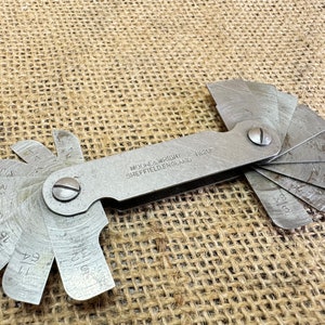 May include: A silver metal angle gauge with a fan of blades marked with fractions of an inch. The gauge is labelled "Moore & Wright Sheffield England 1120F".