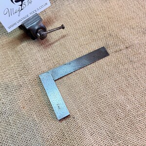 May include: A metal try square with a bevelled edge and a 4 1/2" measurement marked on the blade. The try square is on a hessian surface.