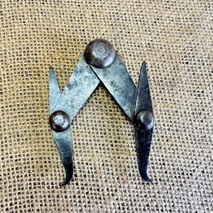 May include: A vintage metal measuring tool with two adjustable arms and rounded ends. The tool is made of silver metal with a worn finish and has two round knobs on the arms.