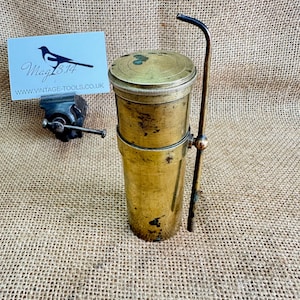 May include: An antique brass oil can with a curved spout and a lid. The can has a cylindrical body and a handle. A small vice and a business card with the text "Mag 13.14" and "www.VINTAGE-TOOLS.co.uk" are also visible.