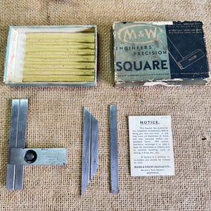 Op de afbeelding: Een precisie vierkantset voor ingenieurs met een doos, messen en een kennisgeving. De doos is gemarkeerd met "M&W ENGINEERS' PRECISION SQUARE". De set bevat een vierkant, twee messen en een kennisgeving van MOORE & WRIGHT (Sheffield) LTD.