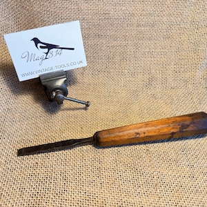 May include: A vintage wood handled chisel with a metal blade, resting on a hessian surface. The chisel is next to a small metal clamp holding a business card with the text "Mag314 www.vintage-tools.co.uk".