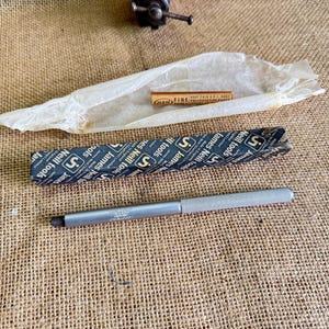 May include: A selection of tools, including a silver metal handle with the text "James Neill tools", a small wooden ruler, and a black and blue package with the text "James Neill tools". The items are on a hessian surface.