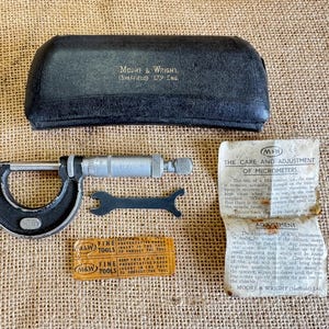 May include: A vintage Moore & Wright micrometer set, including a black case, wrench, and paperwork. The micrometer is silver and black, with "M&W FINE TOOLS" on the packaging. The case is black and has the text "MOORE & WRIGHT (SHEFFIELD) LTD ENG."