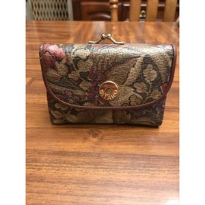 May include: A rectangular wallet featuring a multi-colored floral tapestry pattern in shades of brown, green, and red. The wallet has a gold-tone metal kiss-lock closure at the top and a circular gold-tone emblem on the front flap with the text GITANO.