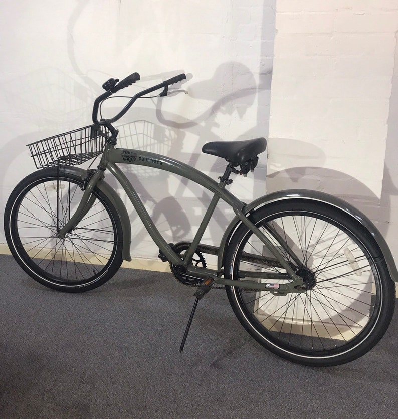 May include: A green cruiser bicycle with black components, including a basket, seat, and tyres with white sidewalls. The bike has a curved frame and mudguards. The text "paul frank" is visible on the frame.