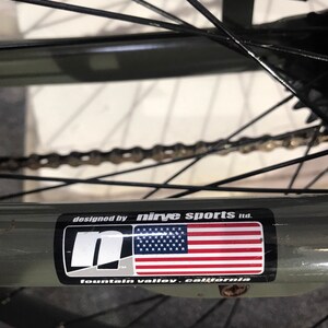 May include: Close-up of a bicycle wheel with a sticker that reads "designed by Nirve Sports Ltd." The sticker features the American flag and the text "fountain valley, california."