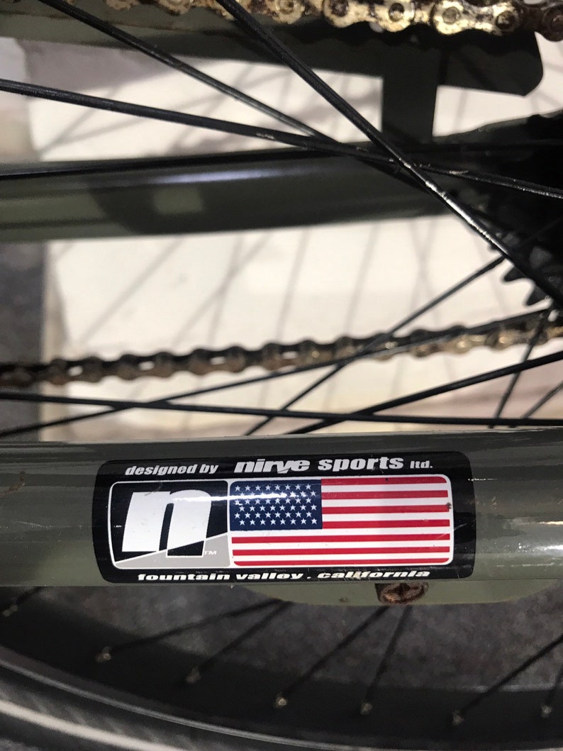 May include: Close-up of a bicycle wheel with a sticker that reads "designed by Nirve Sports Ltd." The sticker features the American flag and the text "fountain valley, california."