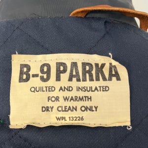 以下が含まれることがあります： 「B-9 Parka」と「quilted and insulated for warmth dry clean only WPL 13226」と黒文字で書かれたベージュのラベルです。