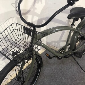 May include: A grey cruiser bicycle with a black wire basket, black handlebars, and a black seat. The bicycle has black tyres with white sidewalls and a bell on the handlebars. The frame has the text "paul frank".