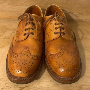 Peut inclure: Une paire de chaussures oxford en cuir beige avec des détails brogues complexes, des bouts fleuris et des lacets assortis. Les chaussures présentent une silhouette basse avec des coutures visibles sur la trépointe et un bout arrondi.