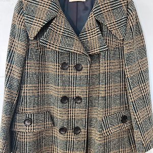 May include: A long, double-breasted coat with a large collar. The coat is made of a plaid fabric in shades of black, brown, and white. The label on the coat reads "Radames Harella".
